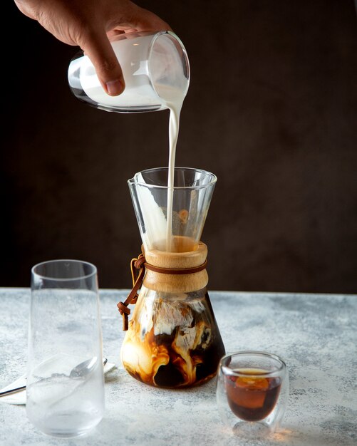 Man pouring milk on coffee in unique shaped glass