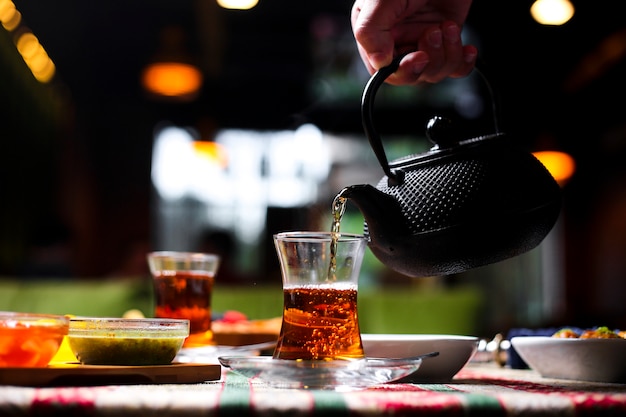 Man pouring tea into armudu glass from stone teapot