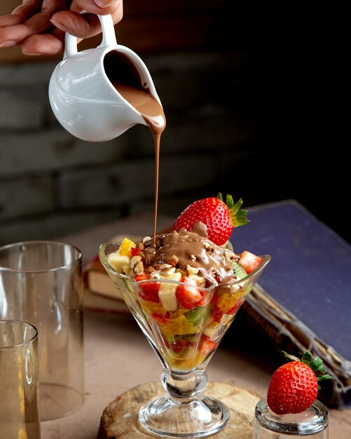 Man pours chocolate on top of fruit salad with nuts