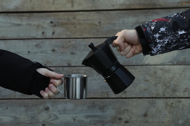A man pours coffee for a man from coffee maker in metal cup