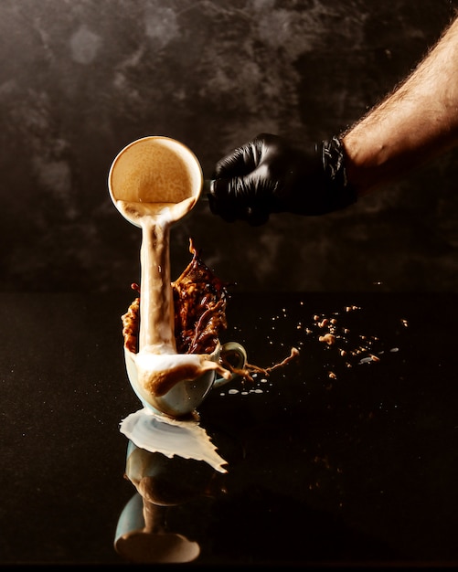 Free photo a man pours from one a cup of coffee into another full cup and coffee spills from the edges