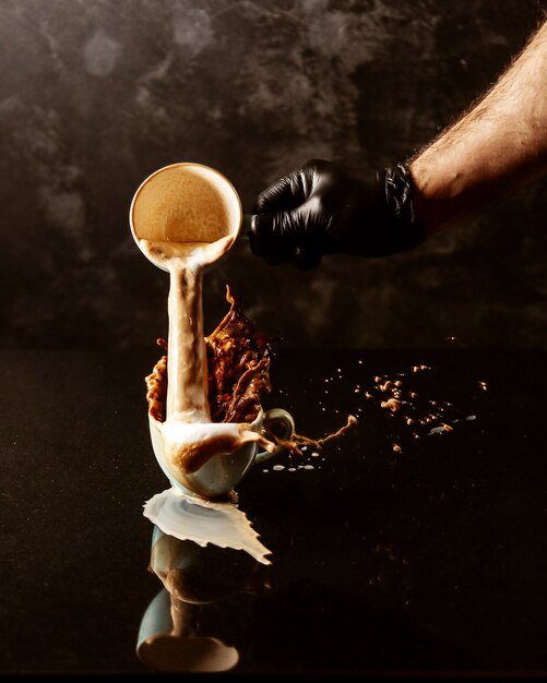 a man pours from one a cup of coffee into another full cup and coffee spills from the edges