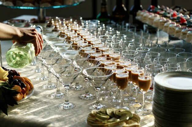 Man pours martini in cocktail glasses on dinner table 