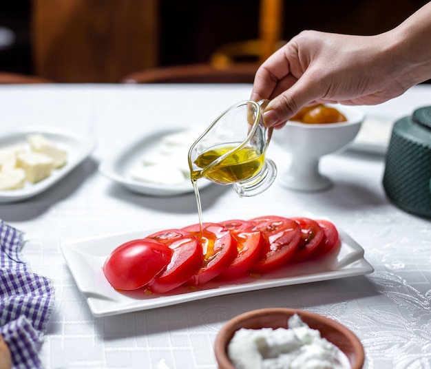 남자는 얇게 썬된 토마토 측면보기에 올리브 오일을 부 어