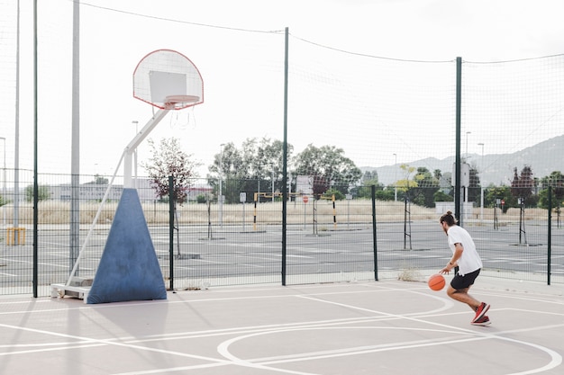 Man practicing basketball near hoop in outdoors court
