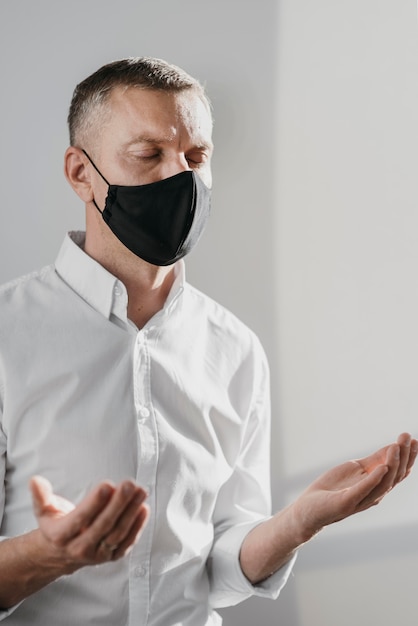 Man praying alone at home while wearing a medical mask