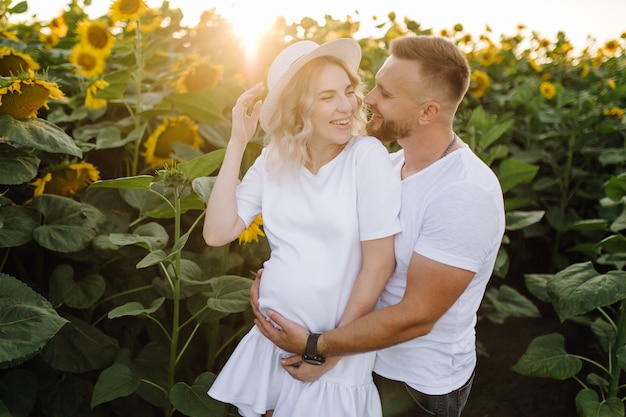 Man and pregnant woman hug each other tender standing in the field with tall sunflowers around them