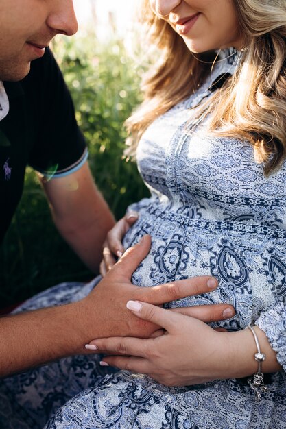 Man and pregnant woman sit together in a green grass full of violet lavender flowers