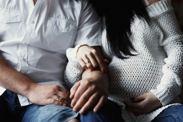 Man and pregnant woman sit on wooden floor holding each other hands 