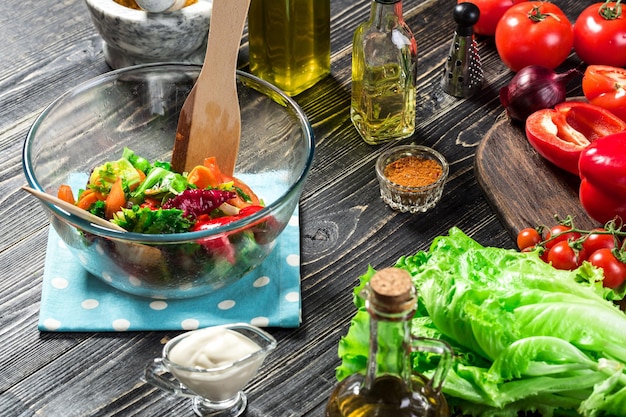 Foto gratuita uomo che prepara insalata con verdure fresche su un tavolo di legno. cucinare cibi gustosi e sani. su sfondo nero. cibo vegetariano, concetto sano o di cucina. avvicinamento