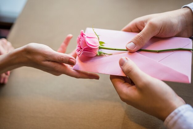 Man presenting envelope and flower to woman 