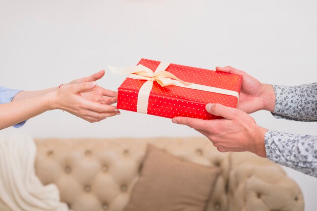 Man presenting gift box to woman near sofa 