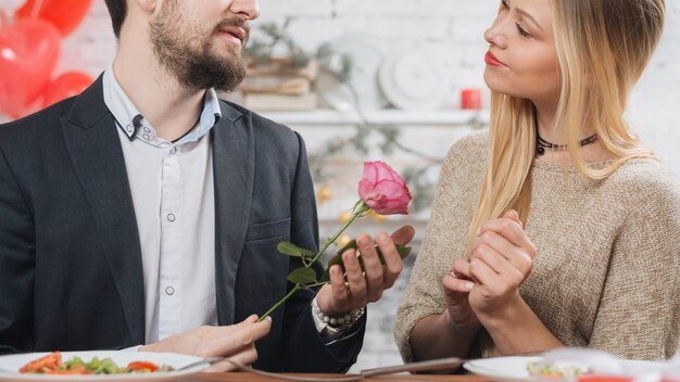 Man presenting pink rose to woman