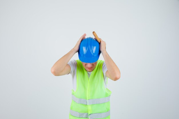 Man pressing hands to ears and holding hammer in construction uniform