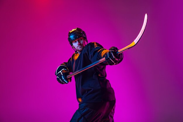 Man professional hockey player training in special uniform with helmet isolated over pink background in neon Winning match