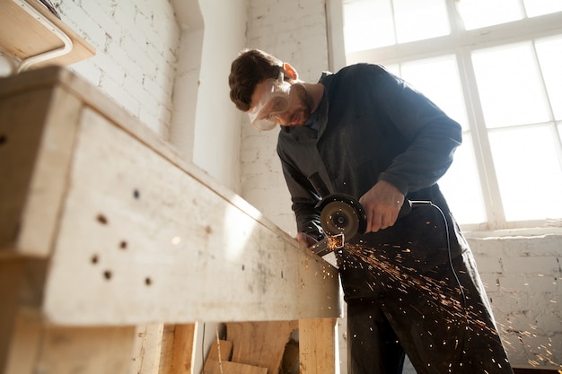 Man in protective glasses using angle grinder for cutting metal