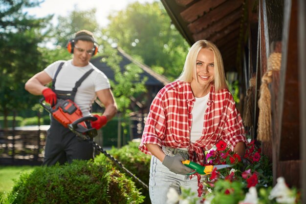 花の世話をしている女性の間に茂みを剪定する男性