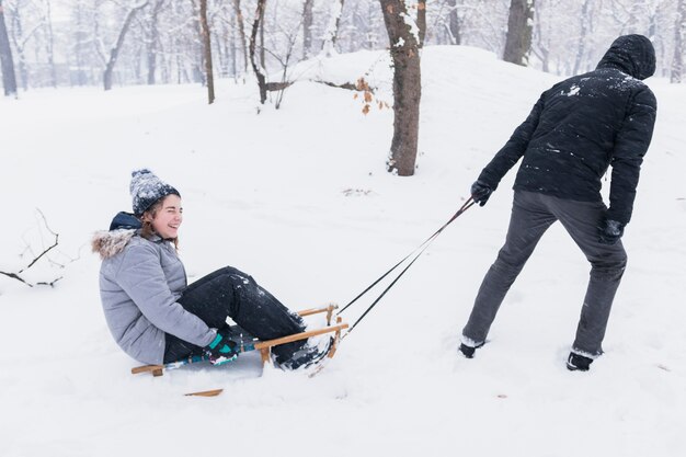 Man pulling smiling girl on sledge through snowy landscape