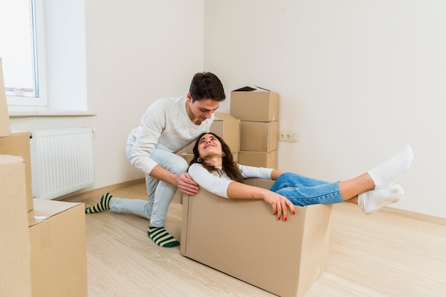 Free photo man pushing the young excited woman sitting inside the cardboard box