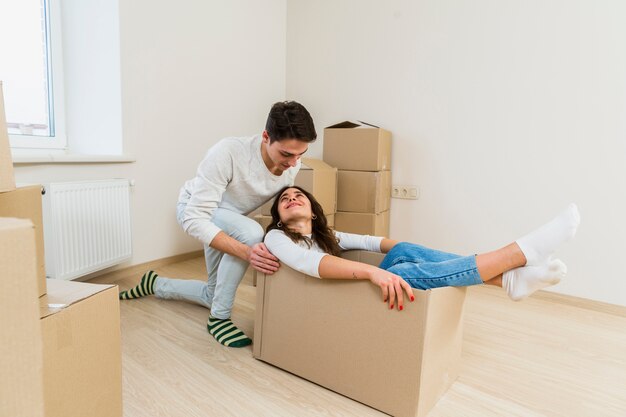 Man pushing the young excited woman sitting inside the cardboard box