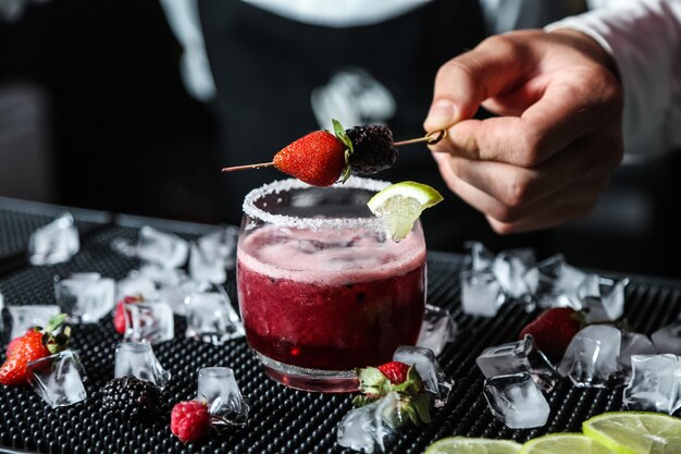 Man puts berry stick on berry cocktail alcohol raspberry blackberry lime ice side view