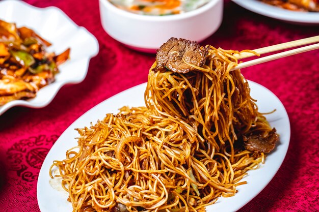 Man puts noodles by sticks onion meat soya sauce side view