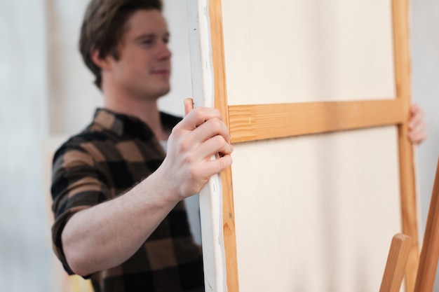 Free photo man putting a canvas on a easel close-up