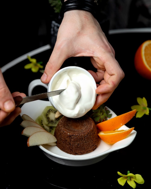 Man putting cream on top of chocolate volcano served with fruit slices