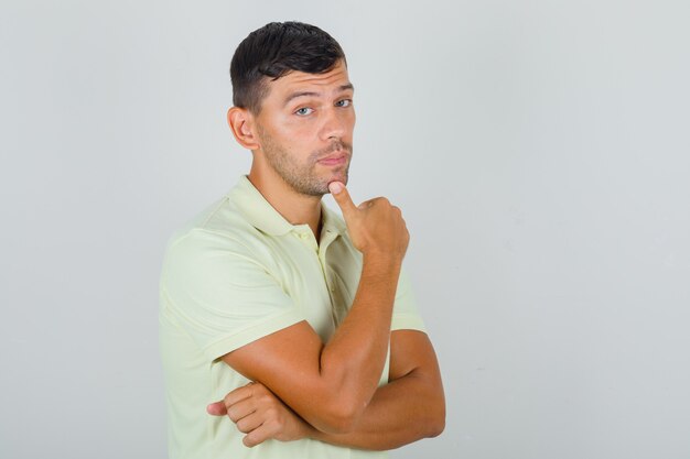 Man putting finger to his chin in yellow t-shirt and looking thoughtful