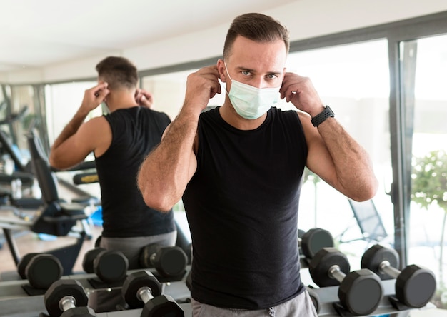 Free photo man putting on medical mask at the gym