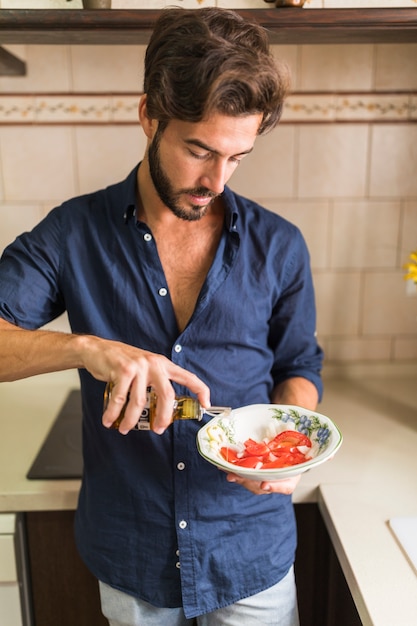 Uomo che mette l'olio d'oliva in una ciotola di insalata