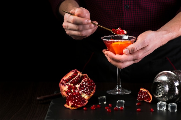 Man putting pomegranate into cocktail glass