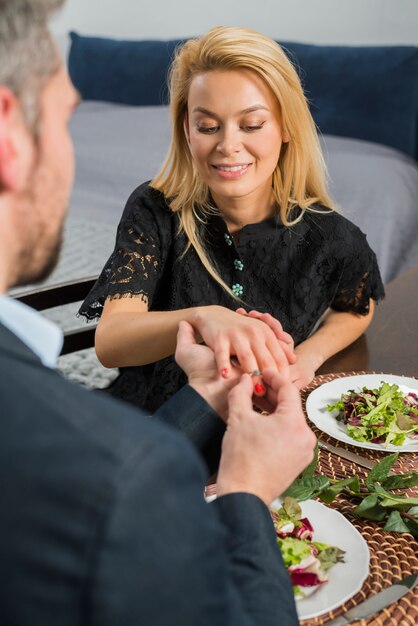 Man putting ring on woman finger at table with dishes 
