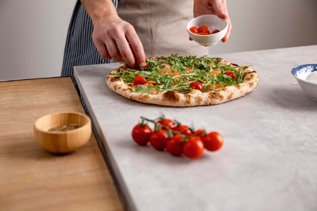 Man putting tomatoes on baked pizza dough with smoked salmon slices