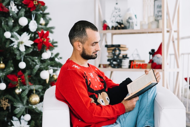 Free photo man reading book near christmas tree