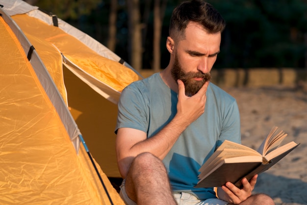 Man reading a book next to tent