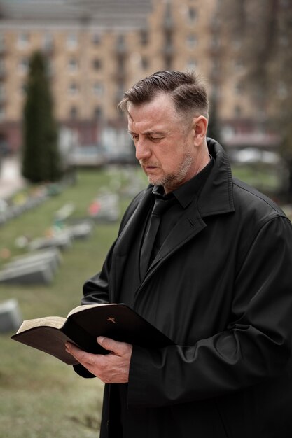 Мужчина читает библию у надгробия на кладбище