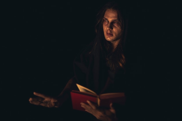 Человек читает красную книгу заклинаний в темноте и смотрит в сторону