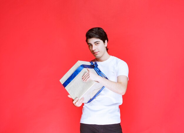 Man receiving and holding a white gift box wrapped with blue ribbon with both hands