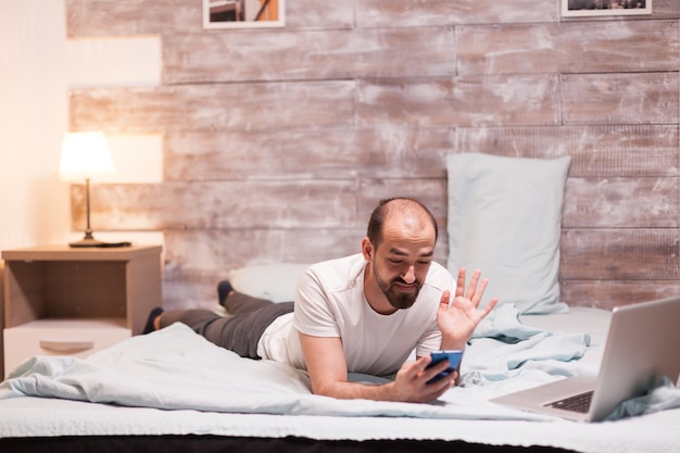 Мужчина принимает видеозвонок поздно ночью во время отдыха в спальне
