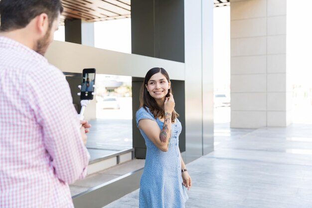 Man recording smiling influencer on smartphone at shopping mall