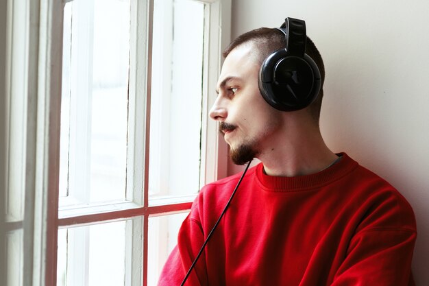 Man in red body shirt listens to the music sitting on the windowsill 