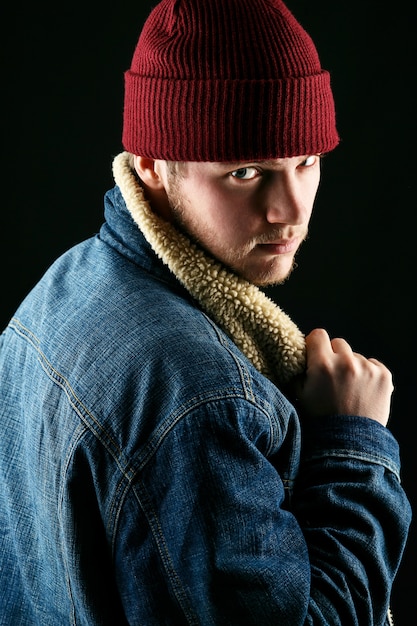 Man in red hat looks over his shoulder posing in jeans jacket 