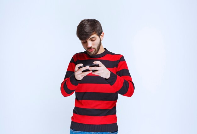 赤い縞模様のシャツを着た男性がスマートフォンでチャットまたはテキストメッセージを送信します。