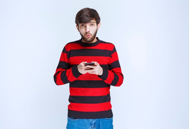 赤い縞模様のシャツを着た男性がスマートフォンでチャットまたはテキストメッセージを送信します。