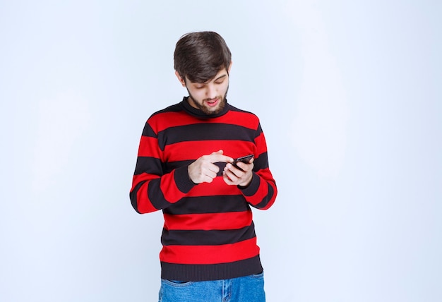 Man in red striped shirt chatting or texting at his smartphone.