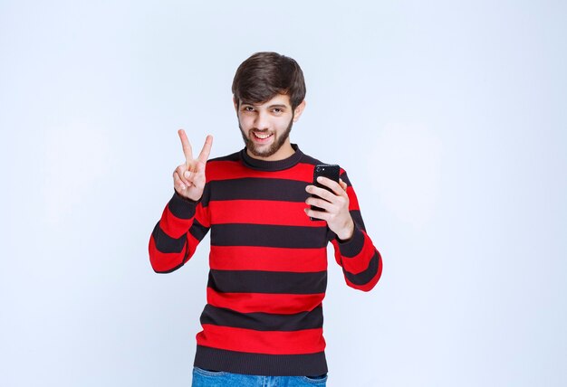 Мужчина в красной полосатой рубашке держит черный смартфон и показывает, что ему нравятся новые функции.