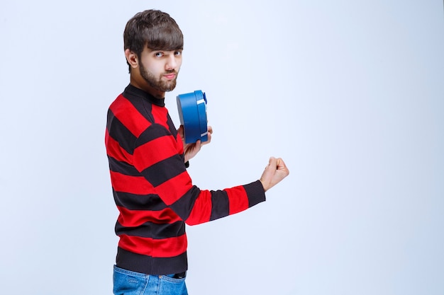 Man in red striped shirt holding a blue heart shape gift box and showing his fist.