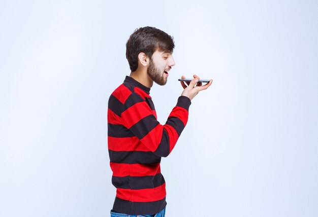 그의 입에 전화를 들고 음성 메시지를 보내는 빨간 줄무늬 셔츠에 남자.