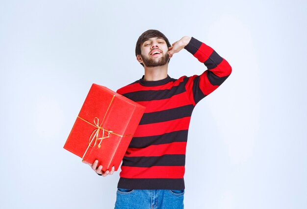 Man in red striped shirt holding a red gift box and calling for someone to deliver it.